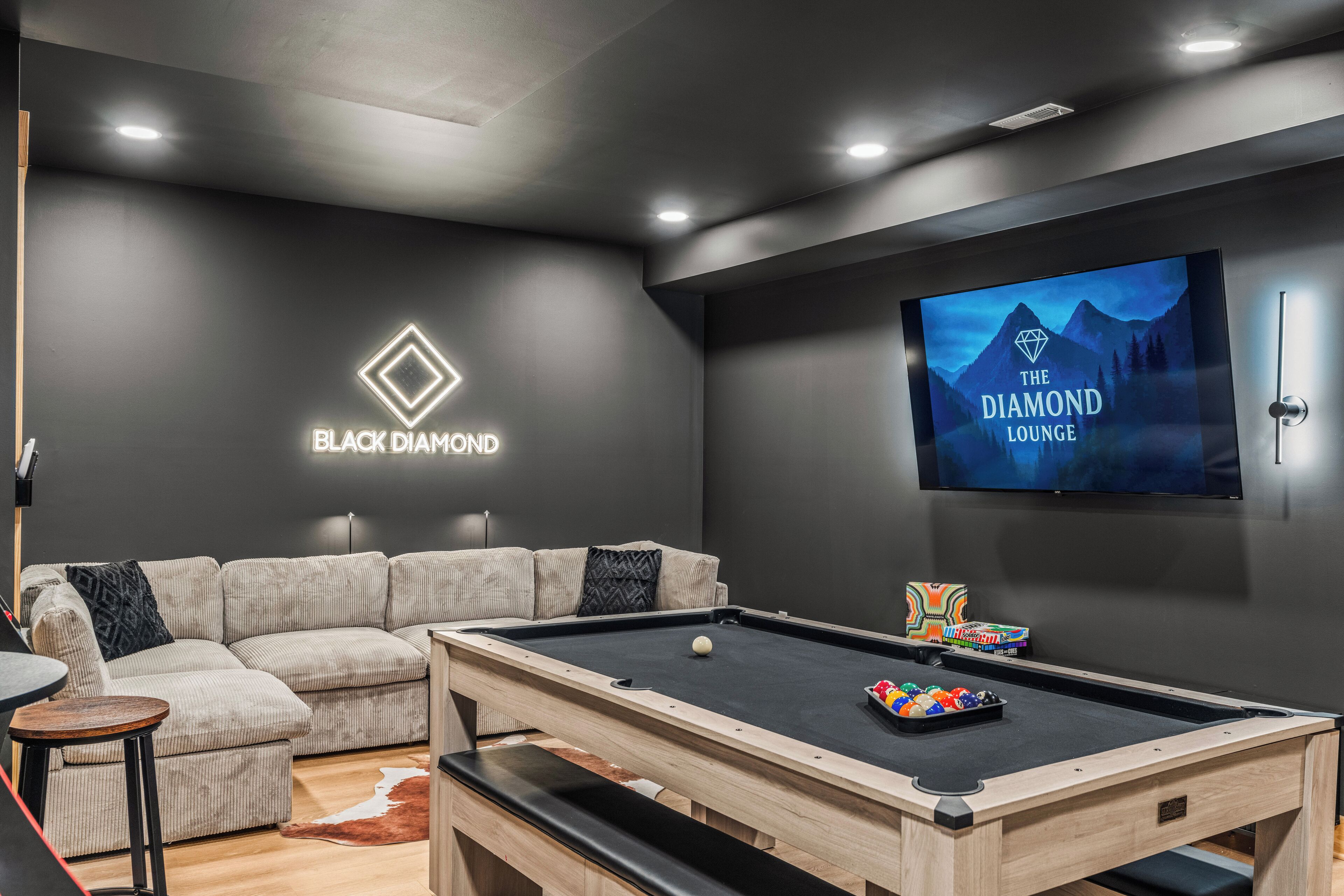 Un salon moderne équipé d’une table de billard, d’un canapé et d’un téléviseur affichant le logo de « The Diamond Lounge ».