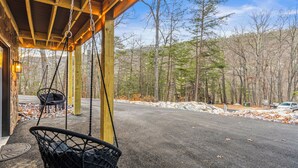 A covered porch with a swing chair, a stone wall, and a view of a forested area. - Black Diamond Retreat 7BR Sleeps 18 Hot Tub+Sauna 3 Min to Massanutten Slopes (McGaheysville)