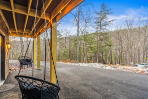 Eine überdachte Veranda mit einer Schaukel, einer Steinmauer und Blick ins bewaldete Gelände.