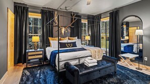 A modern bedroom with a large bed, a ceiling fan, and a view of the outdoors. - Black Diamond Retreat 7BR Sleeps 18 Hot Tub+Sauna 3 Min to Massanutten Slopes (McGaheysville)