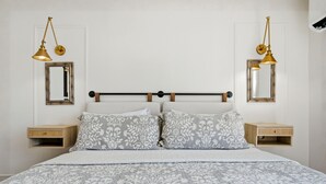 Quarto com cama, duas mesas de cabeceira, duas luminárias na parede e dois espelhos.