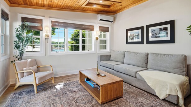 Uma sala de estar com teto de madeira, sofá cinza, mesa de centro de madeira e uma cadeira.