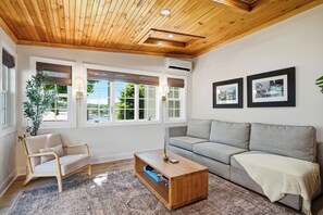A living room with a wooden ceiling, a grey sofa, a wooden coffee table, and a chair. - Boothbay Harbor King Suite - Room 2 at Greenleaf Inn - Balcony, Harbor Views! (Boothbay Harbor)