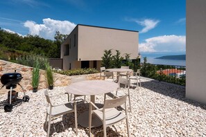 A modern outdoor seating area with a view of the sea, a barbecue grill, and a stone pathway. - Casa Meer an sea-view retreat with panoramic pool (Zagorje)