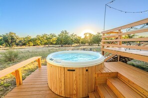 Een houten terras met een jacuzzi, houten banken en een picknicktafel.