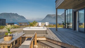 Une terrasse en bois avec un jacuzzi, une table de pique-nique et des chaises longues, le tout offrant une vue sur un paysage montagneux.