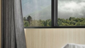 Une chambre d’hôtel avec un lit, une fenêtre avec des rideaux et une vue sur les montagnes et la verdure.