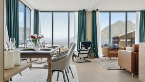 Un espace de repas moderne avec une table dressée pour deux personnes, un canapé et une vue sur les montagnes grâce à de grandes fenêtres.