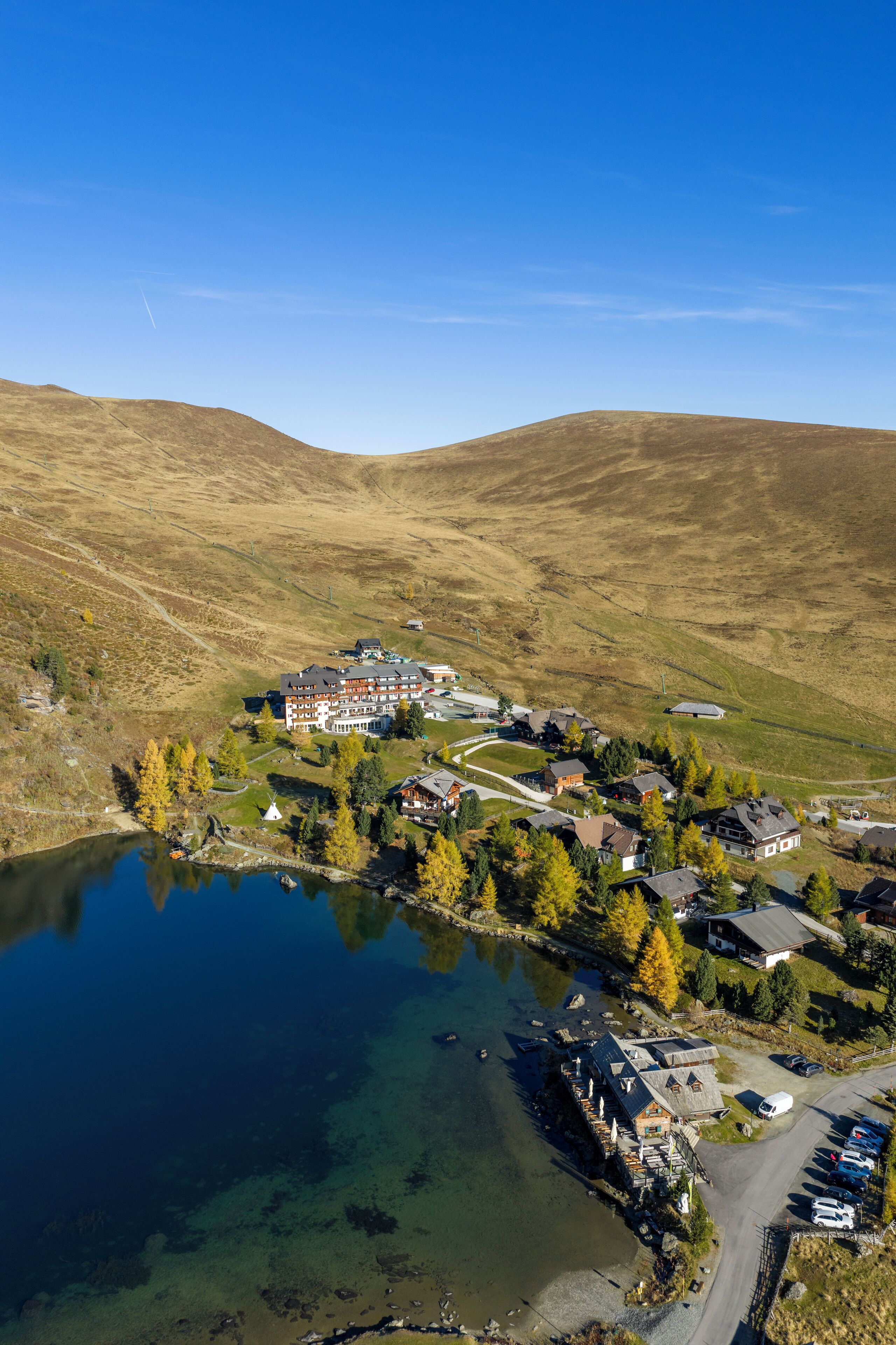 A lakeside resort with multiple buildings, a parking area, and a clear view of the surrounding hills.