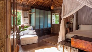 A rustic bedroom with a wooden ceiling, a canopy bed, a white sofa, and a traditional cabinet. - UXUA Alma (Porto Seguro)