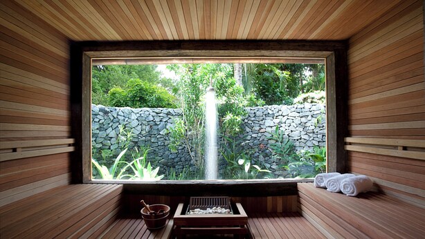 A wooden sauna with a stone wall and a waterfall view. - UXUA Alma (Porto Seguro)