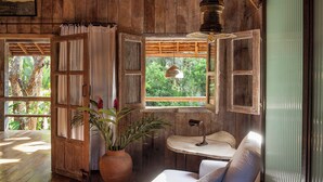 A rustic wooden interior with a white sofa, a large window, and a ceiling with exposed beams. - UXUA Alma (Porto Seguro)