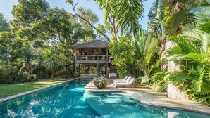 A pool with a wooden deck and lounge chairs, surrounded by lush tropical vegetation. - UXUA Alma (Porto Seguro)