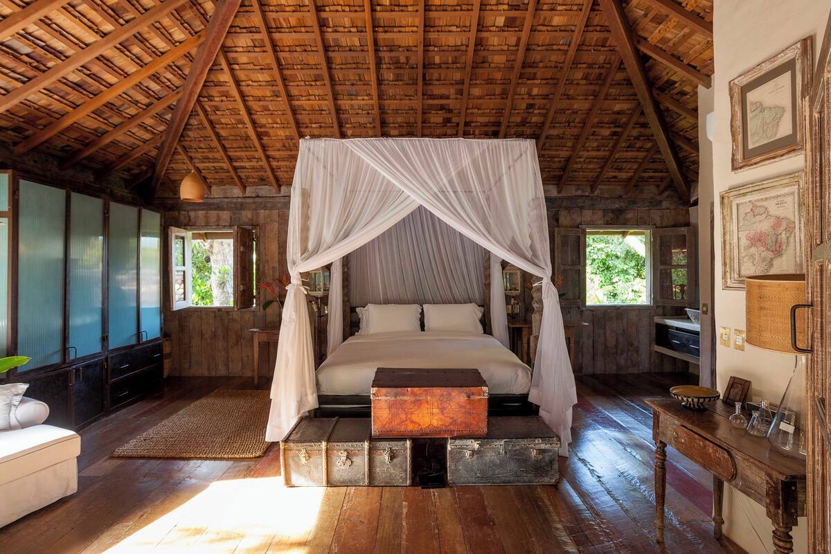A rustic bedroom with a wooden ceiling, a four-poster bed, and a wooden bench.
