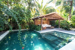 A swimming pool with a wooden pergola and a bench, surrounded by lush greenery. - UXUA Alma (Porto Seguro)
