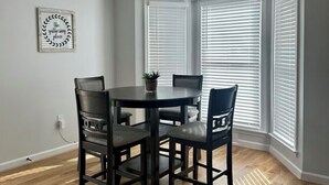 Un comedor con una mesa redonda y cuatro sillas, una planta en maceta sobre la mesa y un cartel en la pared.
