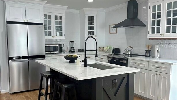 Una cocina moderna con armarios blancos, una isla negra, electrodomésticos de acero inoxidable y piso de madera.