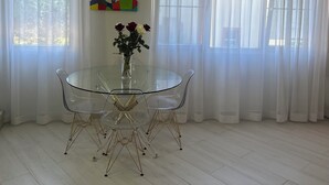 En spiseplads med et glasbord og stole, en lysekrone og et billede på væggen.