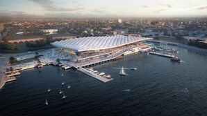 Luchtbeeld van een locatie aan het water met een grote, witte, tentachtige constructie, steigers en boten.