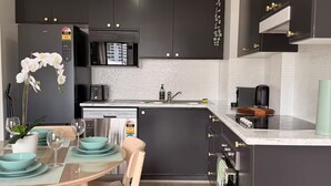 Een moderne keuken met donkere kastjes, een inbouwmagnetron en een eethoek met een tafel gedekt voor twee personen.
