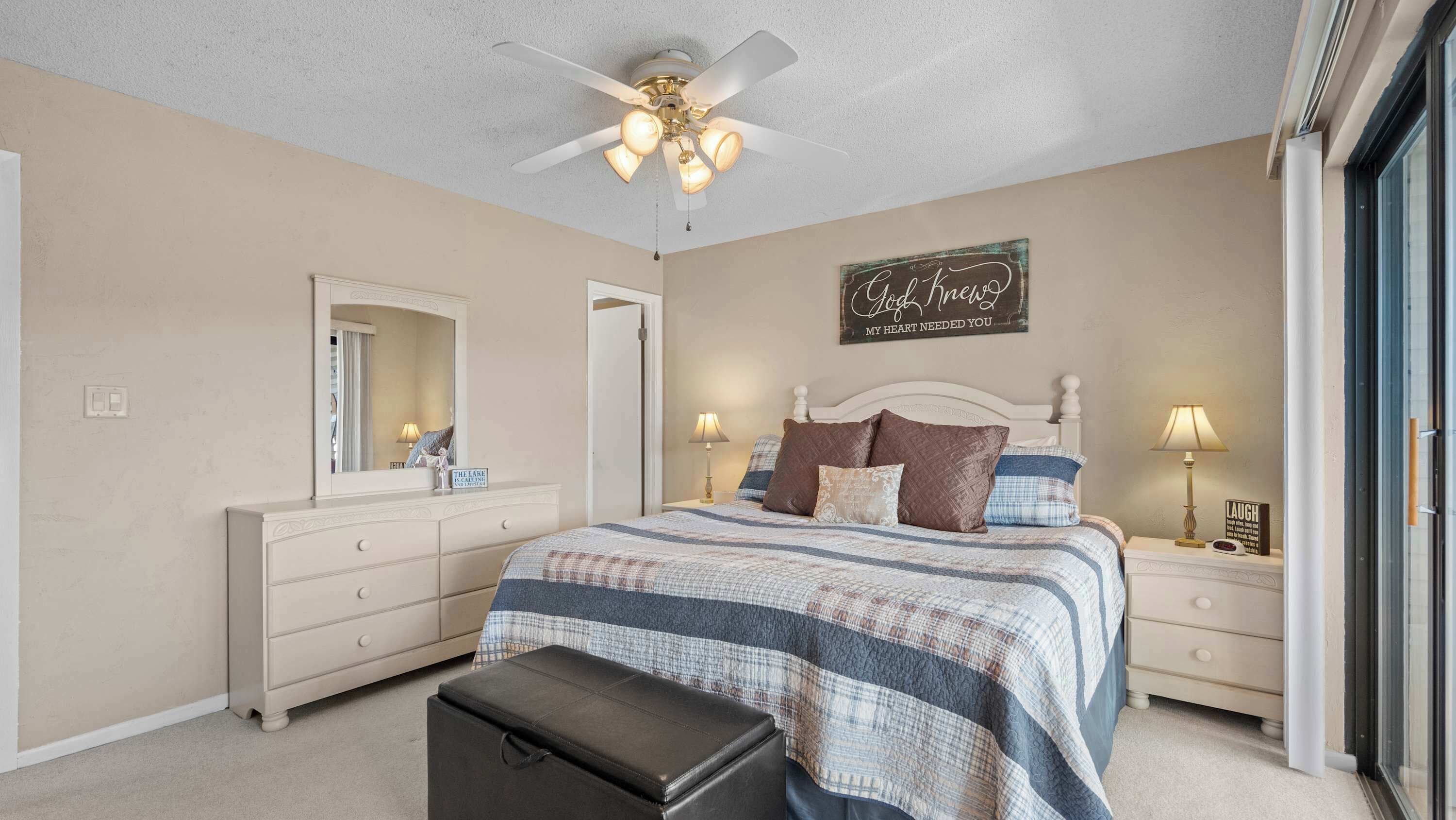 A bedroom with a bed, nightstands, a dresser, a mirror, a ceiling fan, and a window.