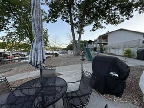 An outdoor patio with a round metal table and chairs, a covered grill, and a swing set in the background. - Easy Breezy Lakefront for 6 (Sunrise Beach)