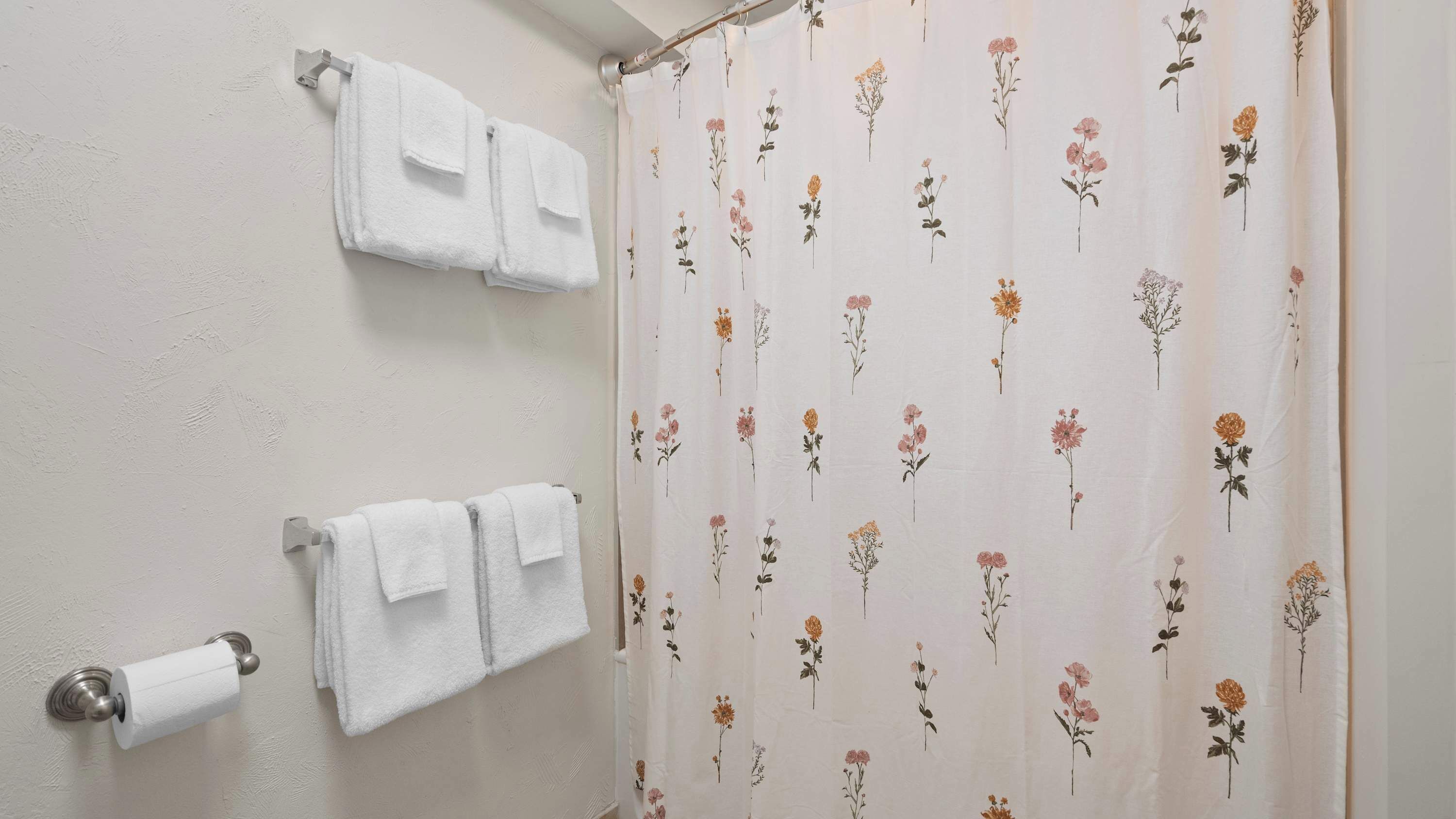 A bathroom with two white towels hanging on a wall-mounted towel rack and a shower curtain with a floral pattern.