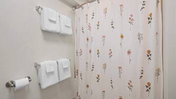 A bathroom with two white towels hanging on a wall-mounted towel rack and a shower curtain with a floral pattern.