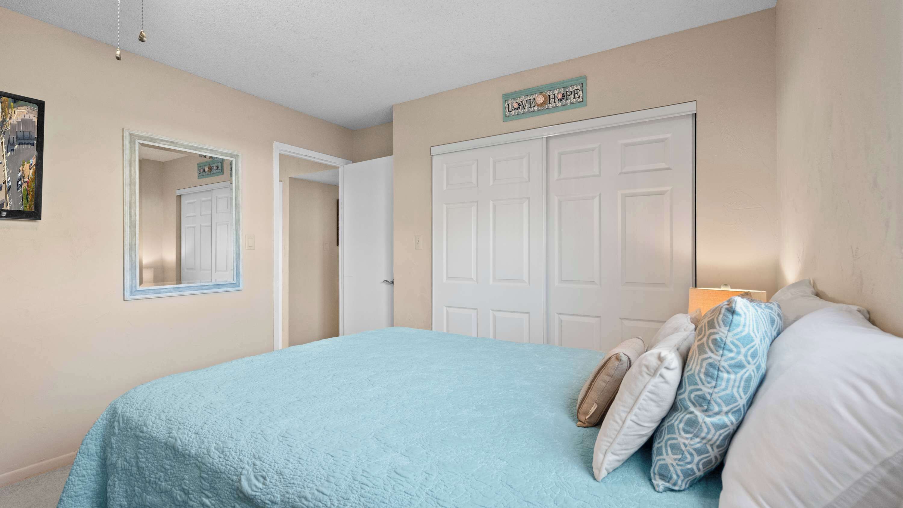 A bedroom with a bed, a door, a mirror, and a wall sign.
