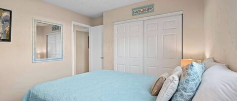 A bedroom with a bed, a door, a mirror, and a wall sign.