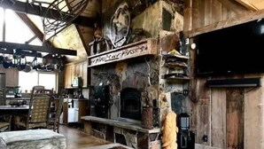 Un intérieur rustique agrémenté d’une cheminée en pierre, de poutres en bois et d’un coin repas avec une table et des chaises.