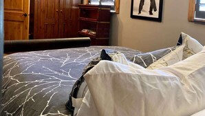 Une chambre à coucher avec un lit, un téléviseur fixé au mur, des meubles en bois et un tableau encadré.