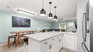 Cocina moderna con armarios blancos, una isla de mármol e iluminación colgante.