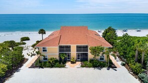 A two-story building with a red roof, surrounded by a sandy beach and a clear blue sea. - Villa Sanibel 1B | Right on the Beach in Sanibel (Sanibel)