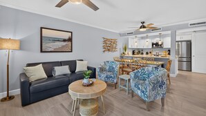 Een moderne woonkamer met een bank, een ronde tafel en stoelen, een eethoek met een tafel en stoelen, en een keuken met kasten en apparatuur.