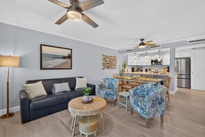 A modern living room with a sofa, round table, and chairs, a dining area with a table and chairs, and a kitchen with cabinets and appliances. - Villa Sanibel 1B | Right on the Beach in Sanibel (Sanibel)