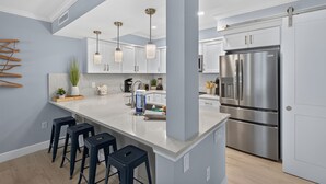 Een moderne keuken met witte kasten, roestvrijstalen apparatuur en een centraal eiland met barstoelen.