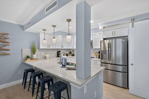 A modern kitchen with white cabinets, stainless steel appliances, and a central island with bar stools. - Villa Sanibel 1B | Right on the Beach in Sanibel (Sanibel)