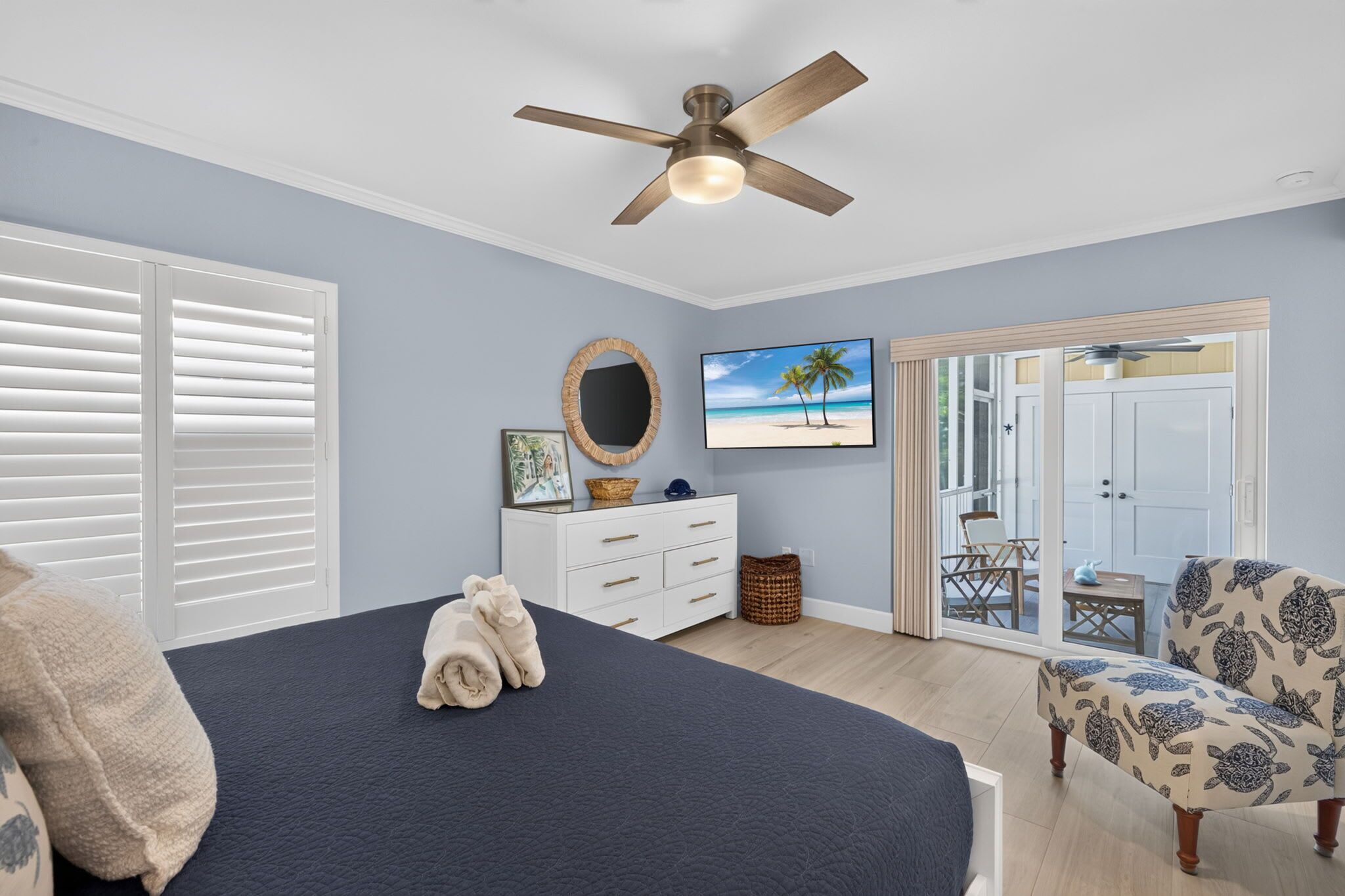 A bedroom with a bed, a ceiling fan, a dresser, a TV, and a view of the outside.