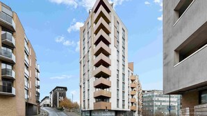 En moderne højhusbygning med en unik zigzag-facade, flere balkoner og en klar himmel.