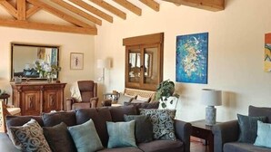 Un salon avec un canapé brun foncé, une table basse en bois et un plafond rustique aux poutres apparentes.