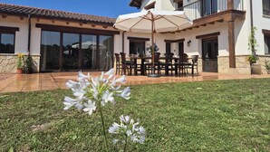 Une vaste terrasse dotée d’un coin repas, d’un grand parasol et offrant une vue sur la maison.