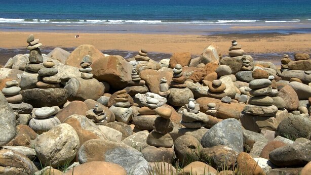 Une plage avec un amas de pierres au premier plan et l’océan en arrière-plan.