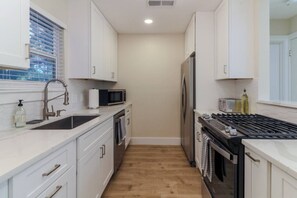 Cocina estrecha con armarios blancos, pileta de acero inoxidable, microondas, refrigerador y estufa a gas.