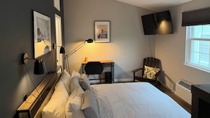 Hotellihuone, jossa on sänky, työpöytä, tuoli, televisio ja taideteos seinällä.