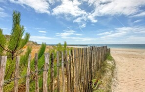 Ein Strand mit einer Holzlattenveranda und Kiefern im Vordergrund.