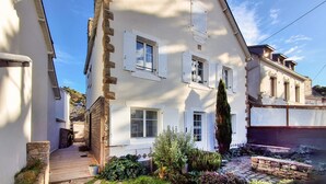 Un bâtiment à deux étages doté d’une façade blanche, de nombreuses fenêtres avec volets et d’un mur d’accent en pierre.