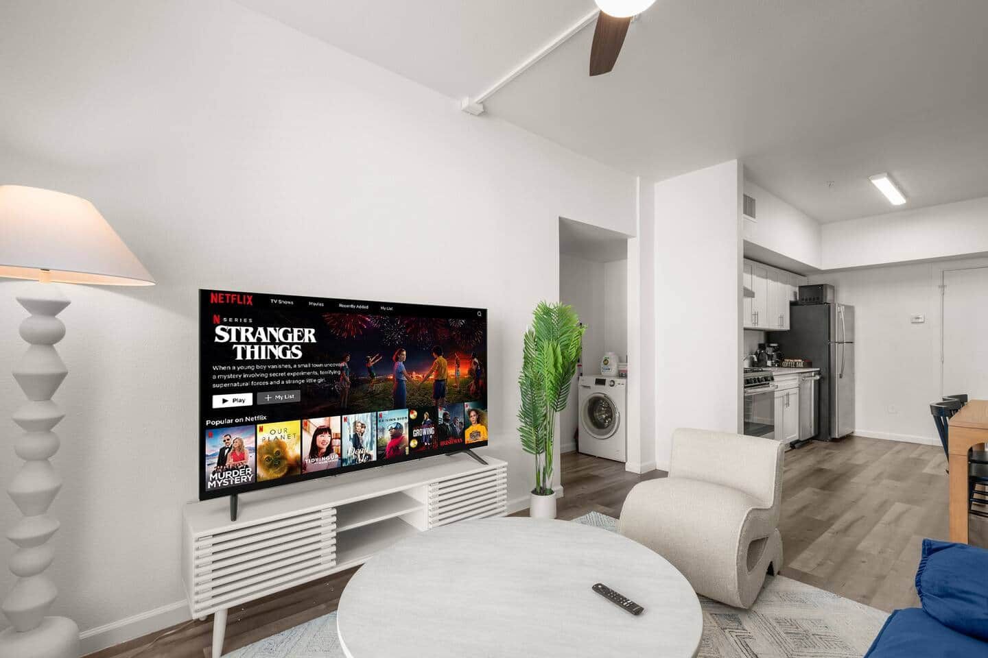 A modern living room with a flat-screen TV displaying a Netflix series, a sofa, a coffee table, and a plant.