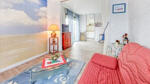 Ein Wohnzimmer mit einem roten Sofa, einem Glastisch, einer Lampe und Wandgemälde von Wolken.