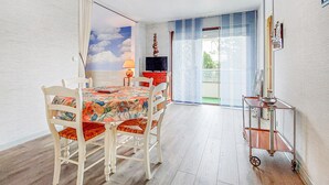 Ein Zimmer mit Esstisch, Stühlen, einem Fernseher und einer Glastür zum Balkon.